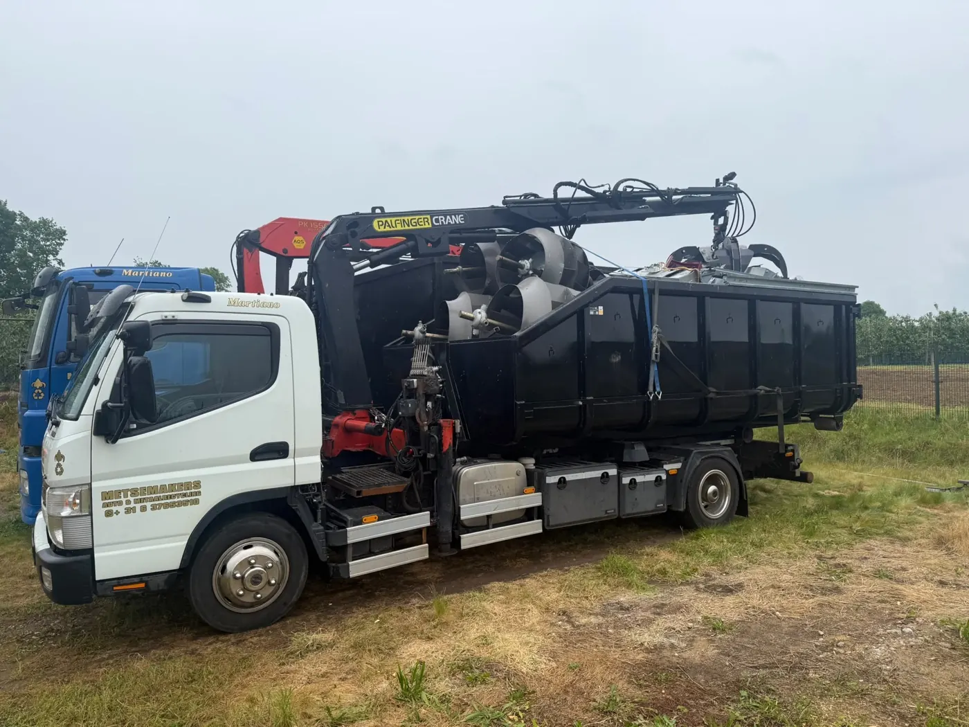 Lkw von Metsemakers mit Ladekran und Container auf einer Wiese